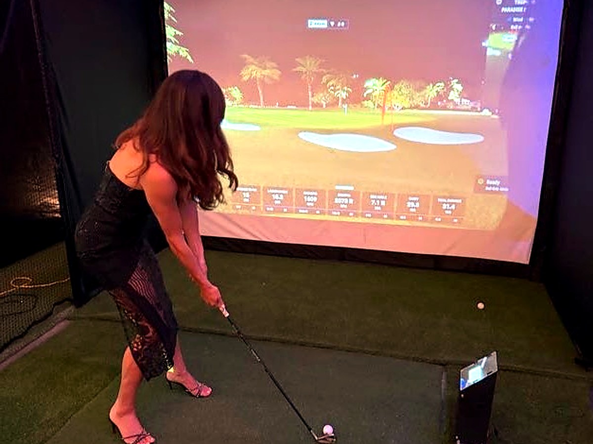 Guest in an evening dress hitting an approach shot on a palm-lined course in the Palmetto Tee Box simulator
