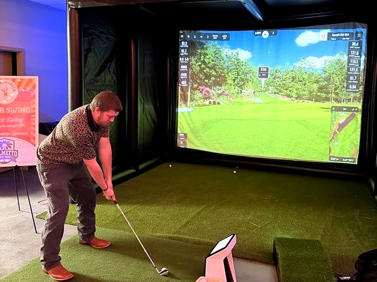 Guest swinging inside the Palmetto Tee Box enclosure set up indoors at an event