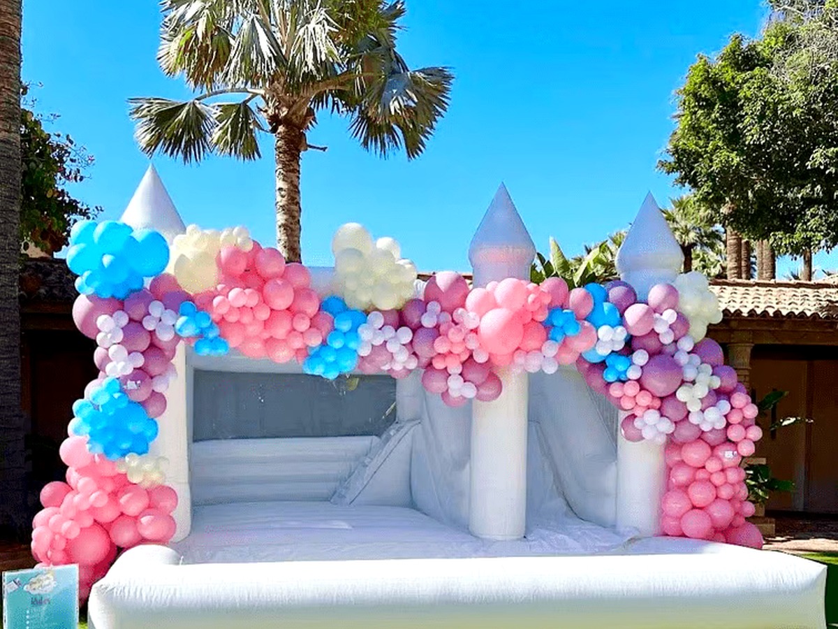 An all-white Hartwell Inflatables castle bounce house with a bishop-top peak, set up as the centerpiece of an outdoor party