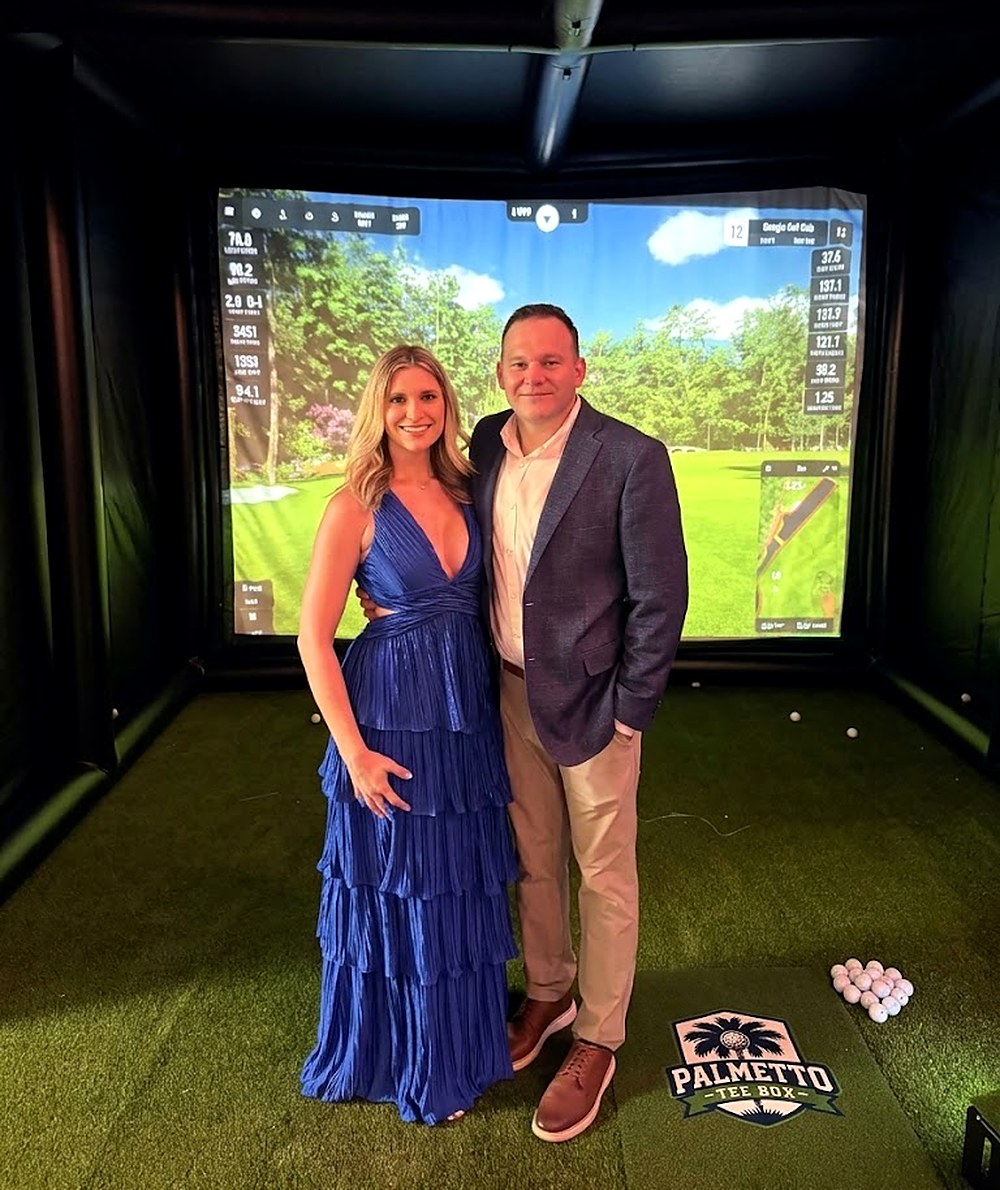 Peter and Meredith standing inside the Palmetto Tee Box simulator bay at an evening event